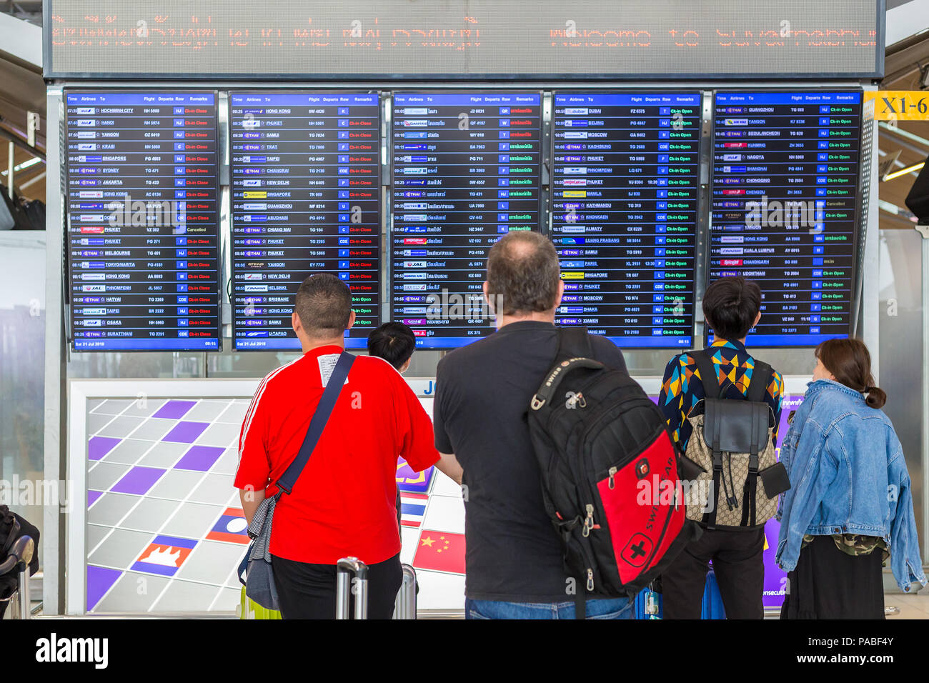 BANGKOK, THAILAND - 21 JULY 2018 - A group of tourists check out their flight schedules on digital display board at Suvarnaphomi International Airport Stock Photo