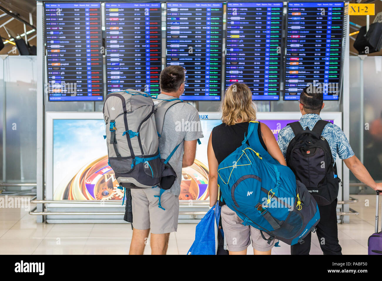 BANGKOK, THAILAND - 21 JULY 2018 - A group of tourists check out their flight schedules on digital display board at Suvarnaphomi International Airport Stock Photo