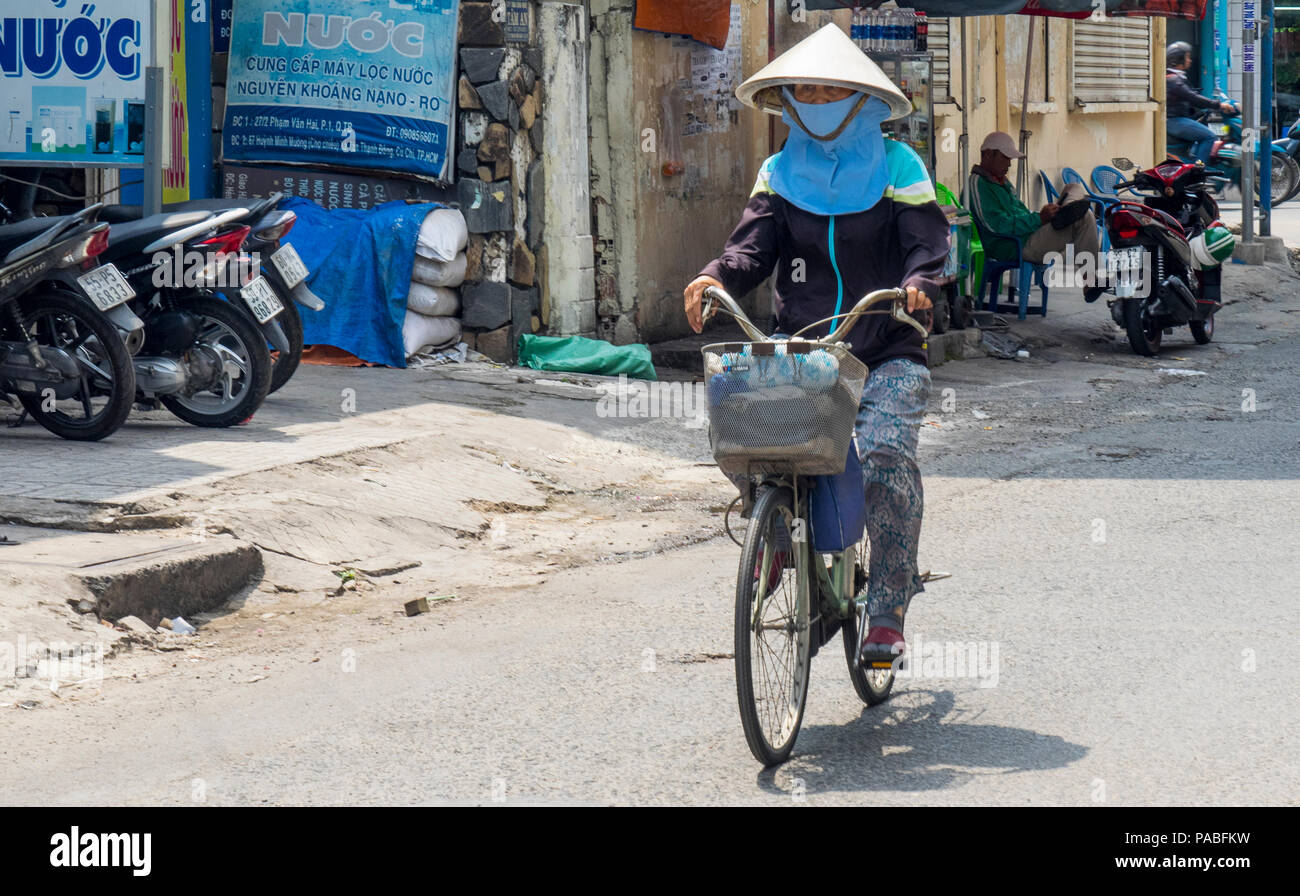 Vietnamese woman wearing a straw conical hat riding a bicycle on a street in Ho Chi Minh City, Vietnam. Stock Photo
