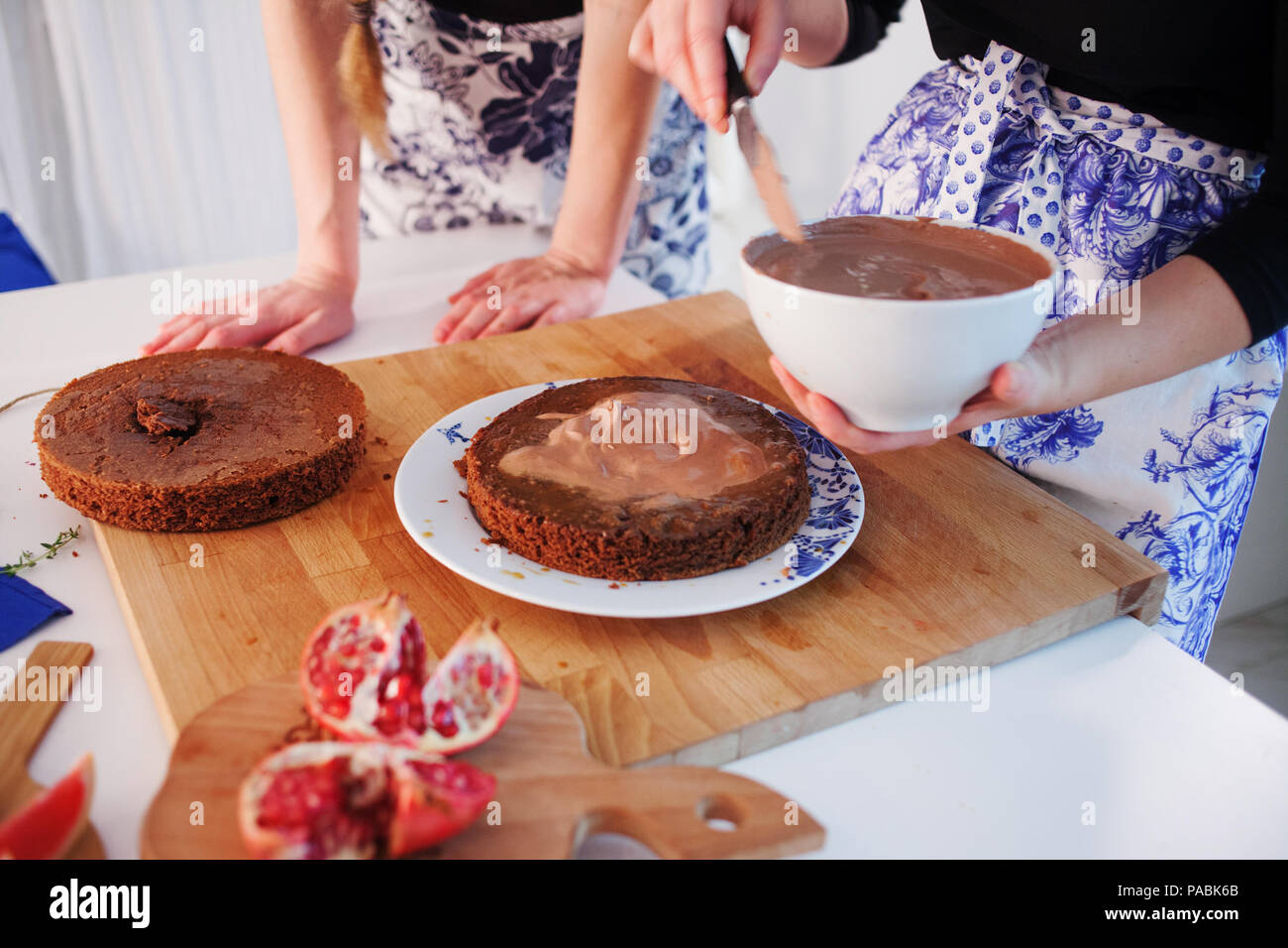 Home confectionery. Two girls making a cake on the kitchen.Women cooking a cake with chocolate cream. Family cooking Stock Photo