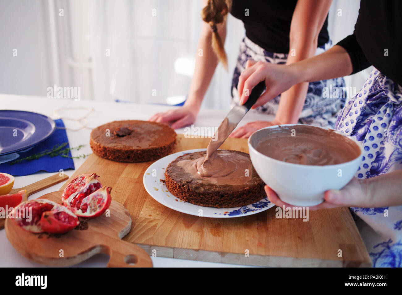 Home confectionery. Two girls making a cake on the kitchen.Women cooking a cake with chocolate cream. Family cooking Stock Photo