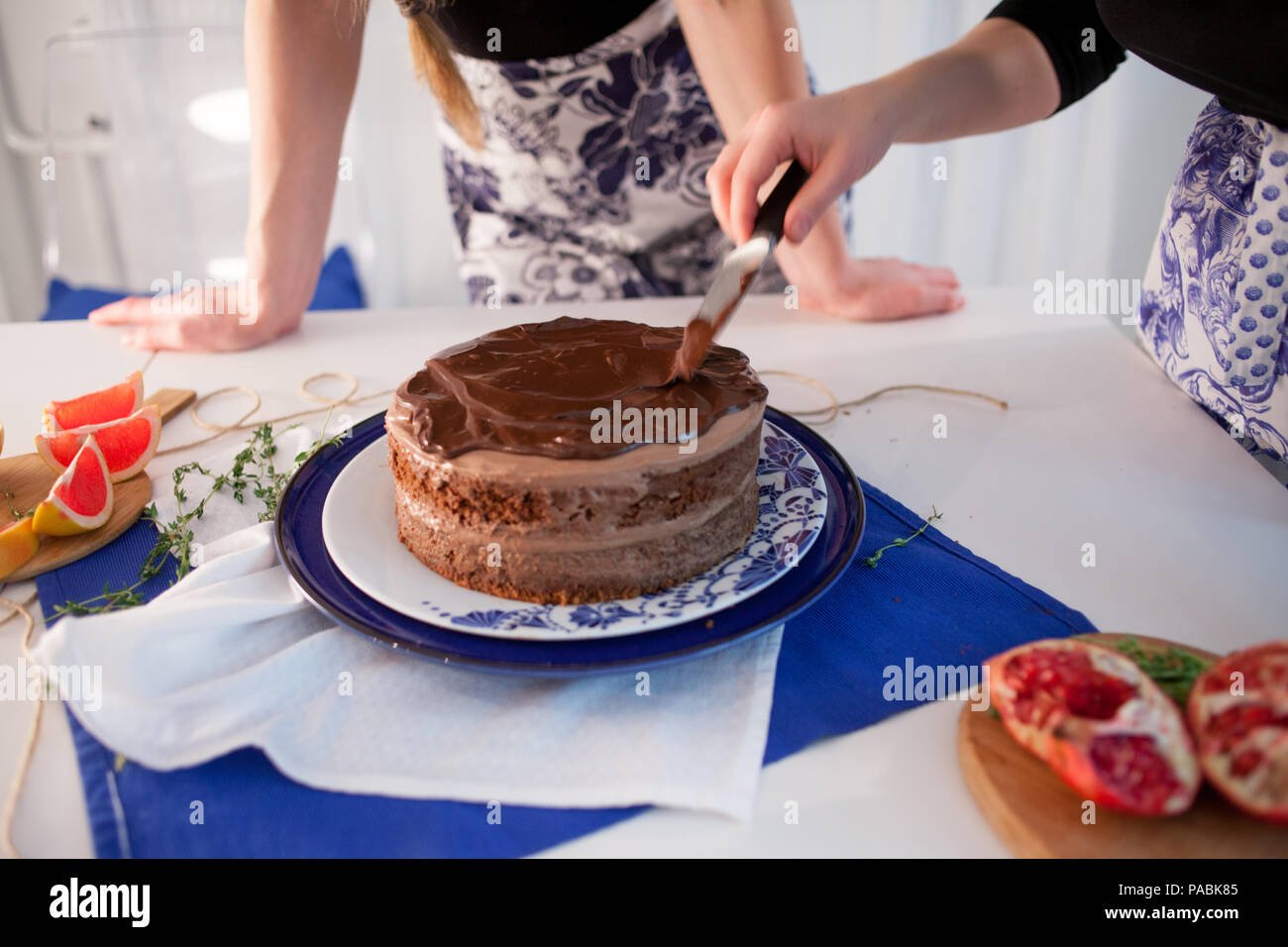 Home confectionery. Two girls making a cake on the kitchen.Women cooking a cake with chocolate cream. Family cooking Stock Photo