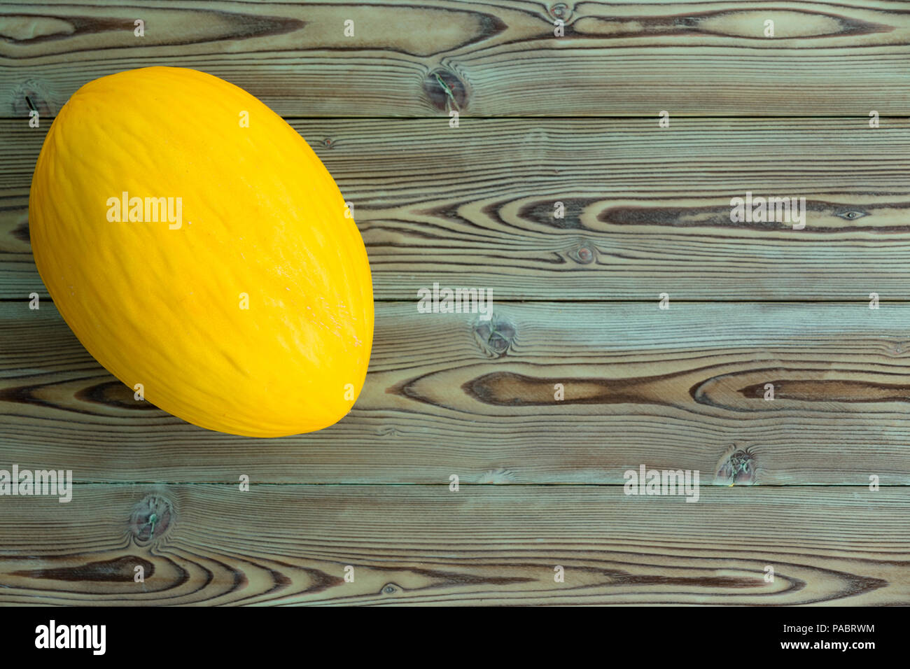 Whole colorful ripe yellow Canary melon, Cucumis melo, on a wooden picnic table ready to be eaten for a refreshing juicy dessert viewed from above wit Stock Photo