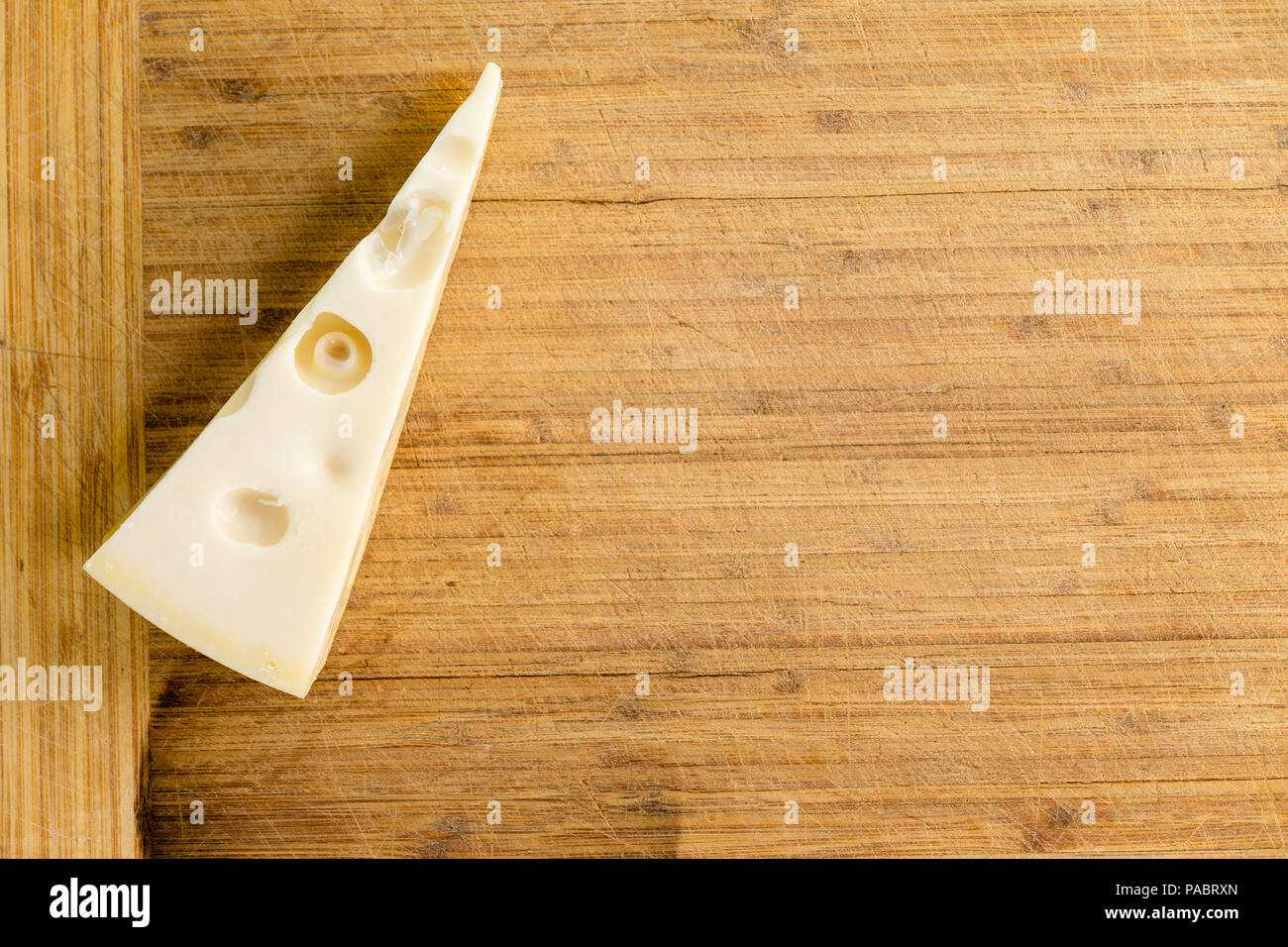 Wedge of traditional Dutch Maasdam cheese with holes on an old wooden bamboo cutting board with copy space ready to cut and serve Stock Photo