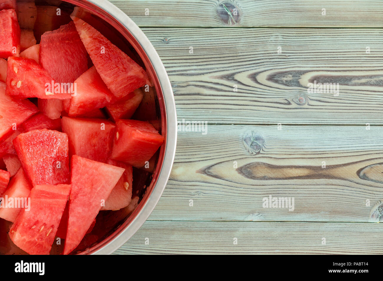 Chilled metal bowl full of diced fresh juicy watermelon for a refreshing summer dessert on a weathered pine wood picnic table with copy space Stock Photo