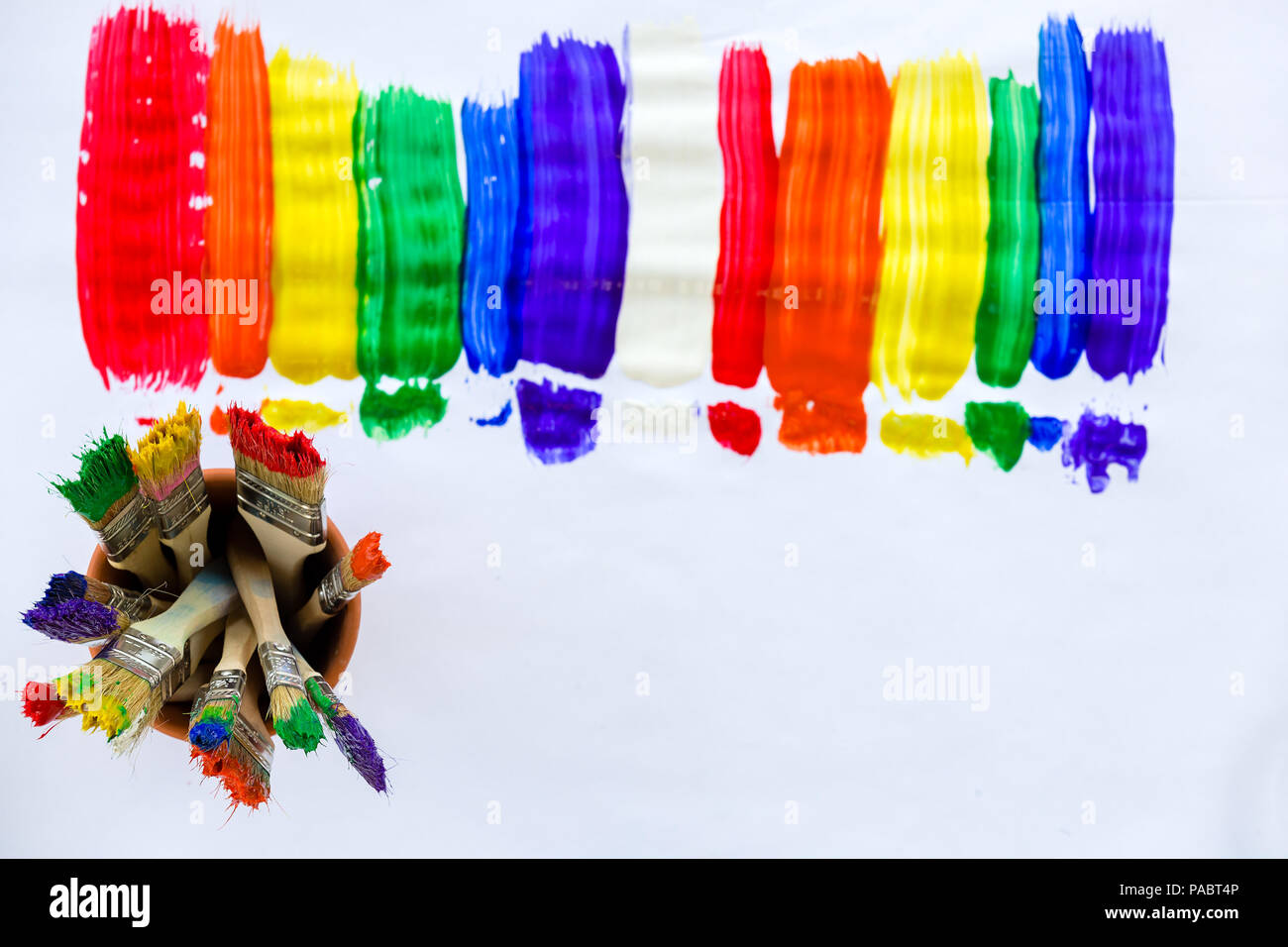 Art and creativity concept with stripes of bright vivid paint in the colors of the rainbow and a jar full of dirty colorful paint brushes forming a fr Stock Photo