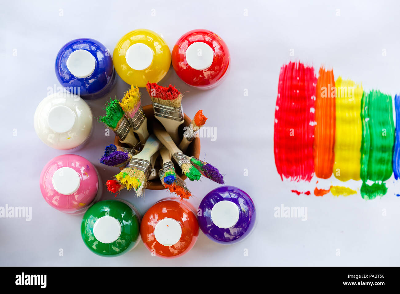 Bottles of colorful paint in the colors of the rainbow arranged in a circle around used paint brushes with vivid bristles viewed from above alongside  Stock Photo