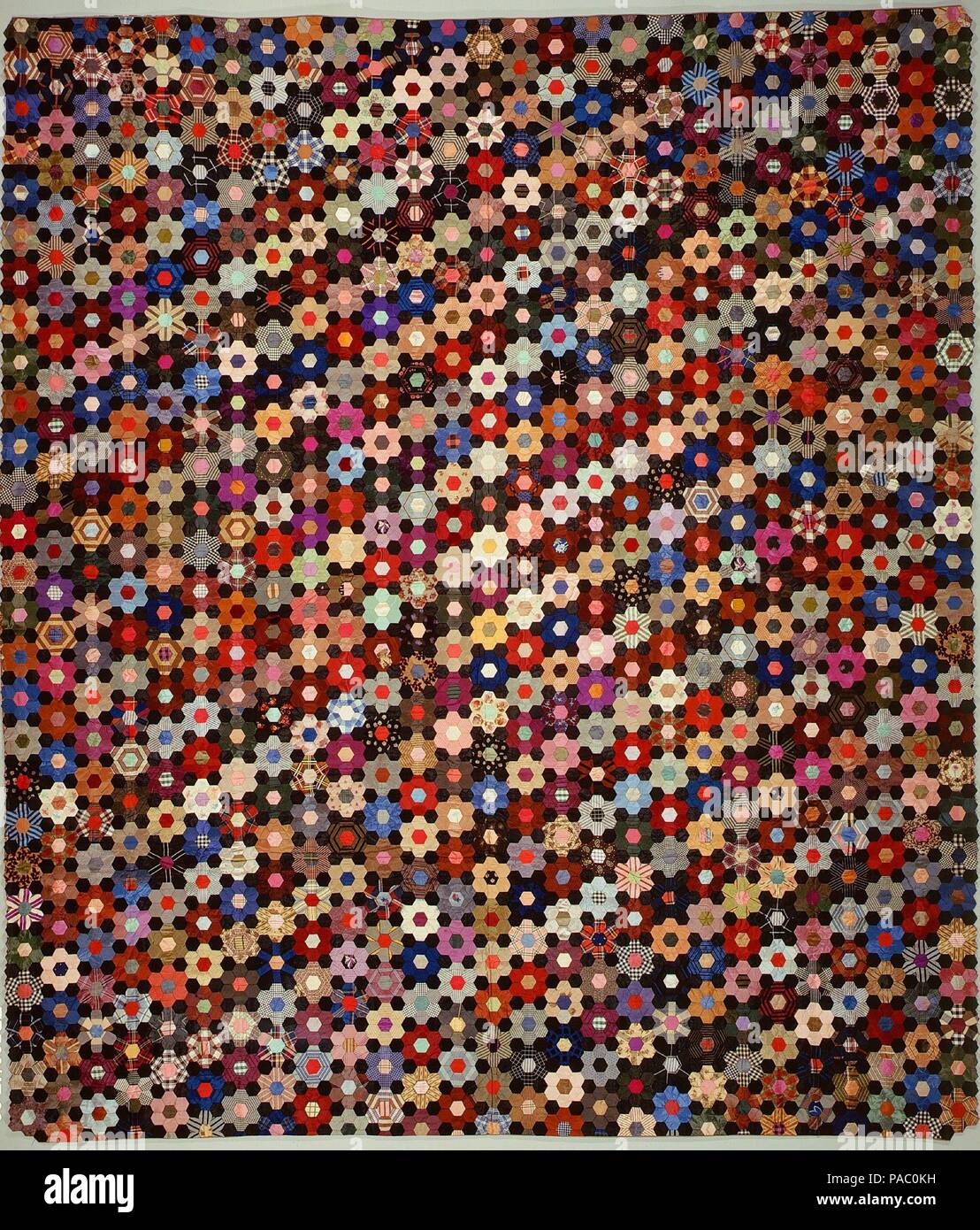 Quilt, Hexagon or mosaic pattern. Culture: American. Dimensions: 87 x 75 1/2 in. (221 x 191.8 cm). Maker: Anne Record (born 1832). Date: begun 1864.  This pieced bed cover has a top composed of hexagons of multicolored silks, including cut velvets, plaids, prints, and brocades. Each colored rosette (made from sewn hexagons) is set off by six surrounding hexagons of plain black silk. The bed cover is unquilted; the batting is attached to the top with an inner layer of brown printed-silk chiffon through which long zigzag running stitches are sewn. The sides are turned under and sewn together. La Stock Photo