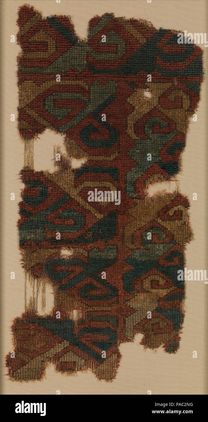 Carpet Fragment. Dimensions: Textile: H. 22 in. (55.9 cm)  W. 11.5 in. (29.2cm)  Mount: H. 27 1/2 in. (69.9 cm)  W. 12 1/2 in. (31.8 cm). Date: 14th-15th century.  This irregular-shaped fragment is decorated with rows of hook motifs and stylized leaves in dark blue, green, and yellow on a red ground. This design once was repeated on a larger surface to fill the main field of an Anatolian carpet. The geometric aspect of the composition relates this fragment to the earlier period (13th-14th centuries; Seljuq and Beyliq periods) of which only few examples survive. The interlocking hocked motifs,  Stock Photo