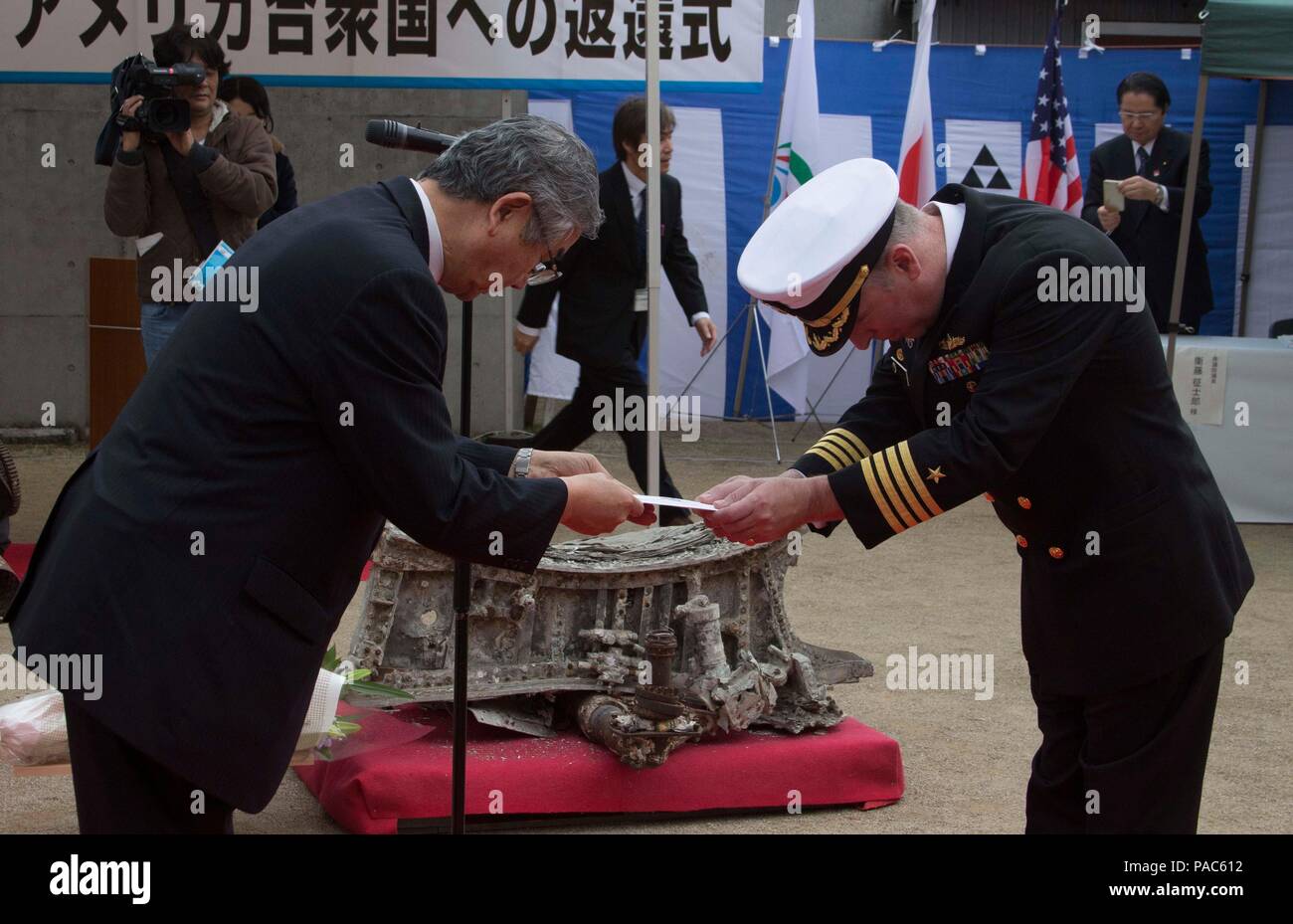SAIKI CITY, Japan (March 6, 2016) Commander U.S. Fleet Activities Sasebo Capt. Matthew Ovios accepts the inventory of parts of a World War II F4U-1D Corsair fighter-bomber from Saiki City Mayor Yasuyoshi Nishijima at the departure ceremony held for the aircraft parts at Yawaragi Peace Memorial Hall in Saiki City, Japan on Mar. 6, 2016. The flowers honor the aircraft’s pilot whose body was never recovered. The parts are from a Fighter Squadron (VF) 10 Corsair that was ditched off Saiki on March 18, 1945 after attacking an Oita military airfield. They were salvaged from the water and displayed u Stock Photo