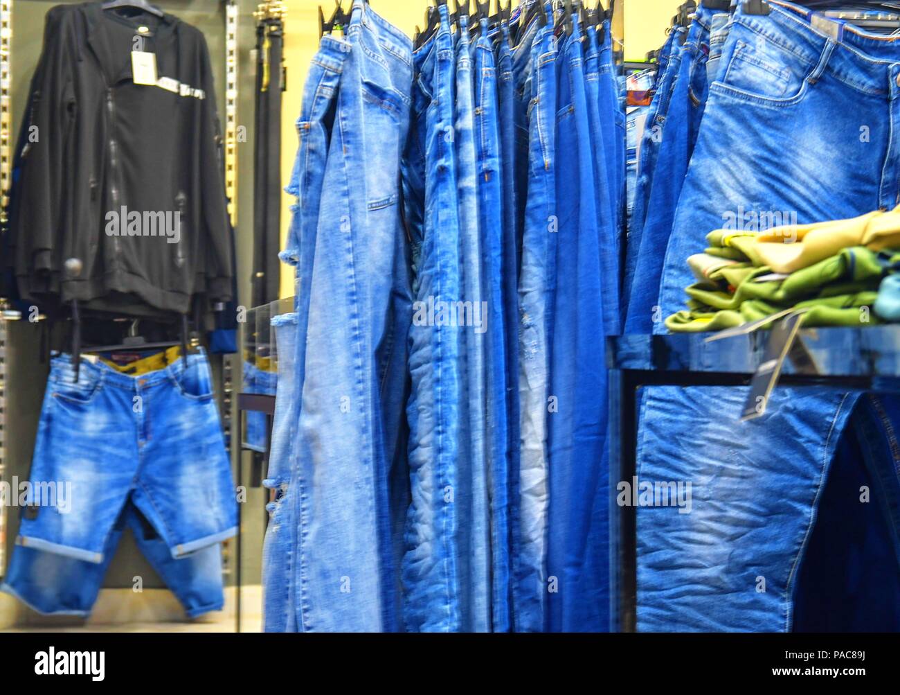 Row of hanged blue jeans in a shop. Clothes store. Shopping in fashion mall. Garments on hangers. Stock Photo