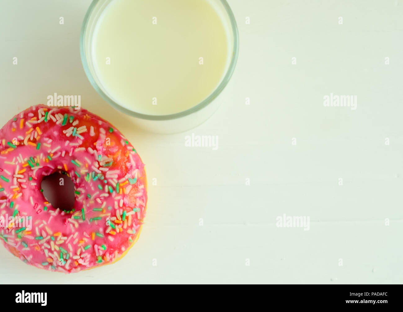 The glass of milk and pink glazed donuts on white wooden background.Sweet donuts.Copyspace right. Stock Photo