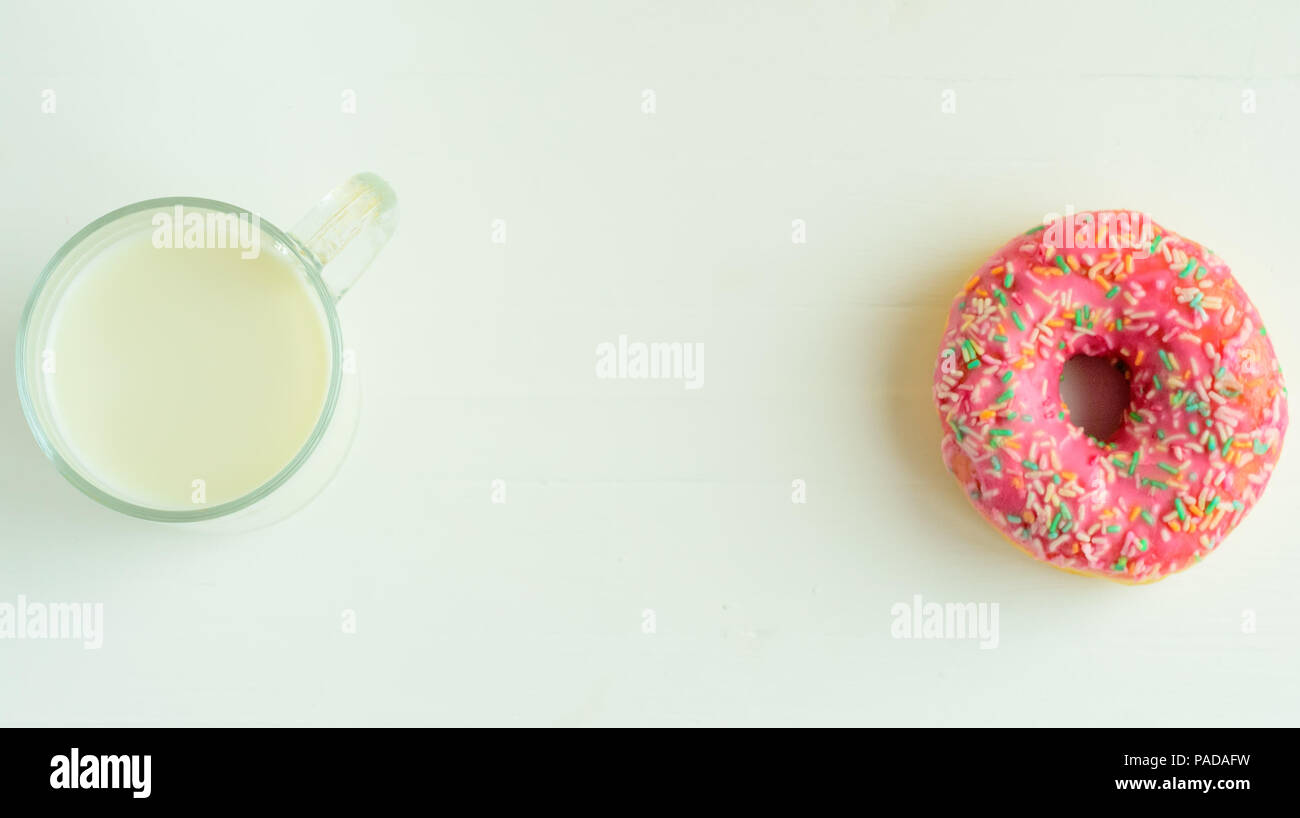 The glass of milk and pink glazed donuts on white wooden background.Sweet donuts.Copyspace middle. Stock Photo