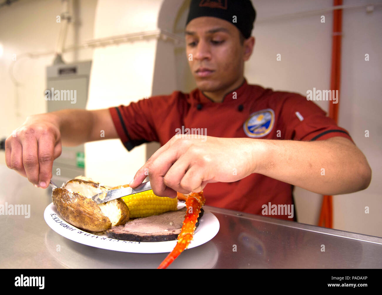 NEWPORT NEWS, Va. (Mar.18, 2016) --  Culinary Specialist Seaman Adrian Palmer, a native of Colombia, S.C, prepares a plate of food for Pre-Commissioning Unit Gerald R. Ford (CVN 78) Sailors taking part in a March birthday meal celebration on the ship's mess decks.  Ford is scheduled for commissioning in 2016.  (U.S. Navy photo by Mass Communication Specialist 1st Class Patrick Grieco/Released) (This image was altered for security purpose by blurring out security badges) Stock Photo