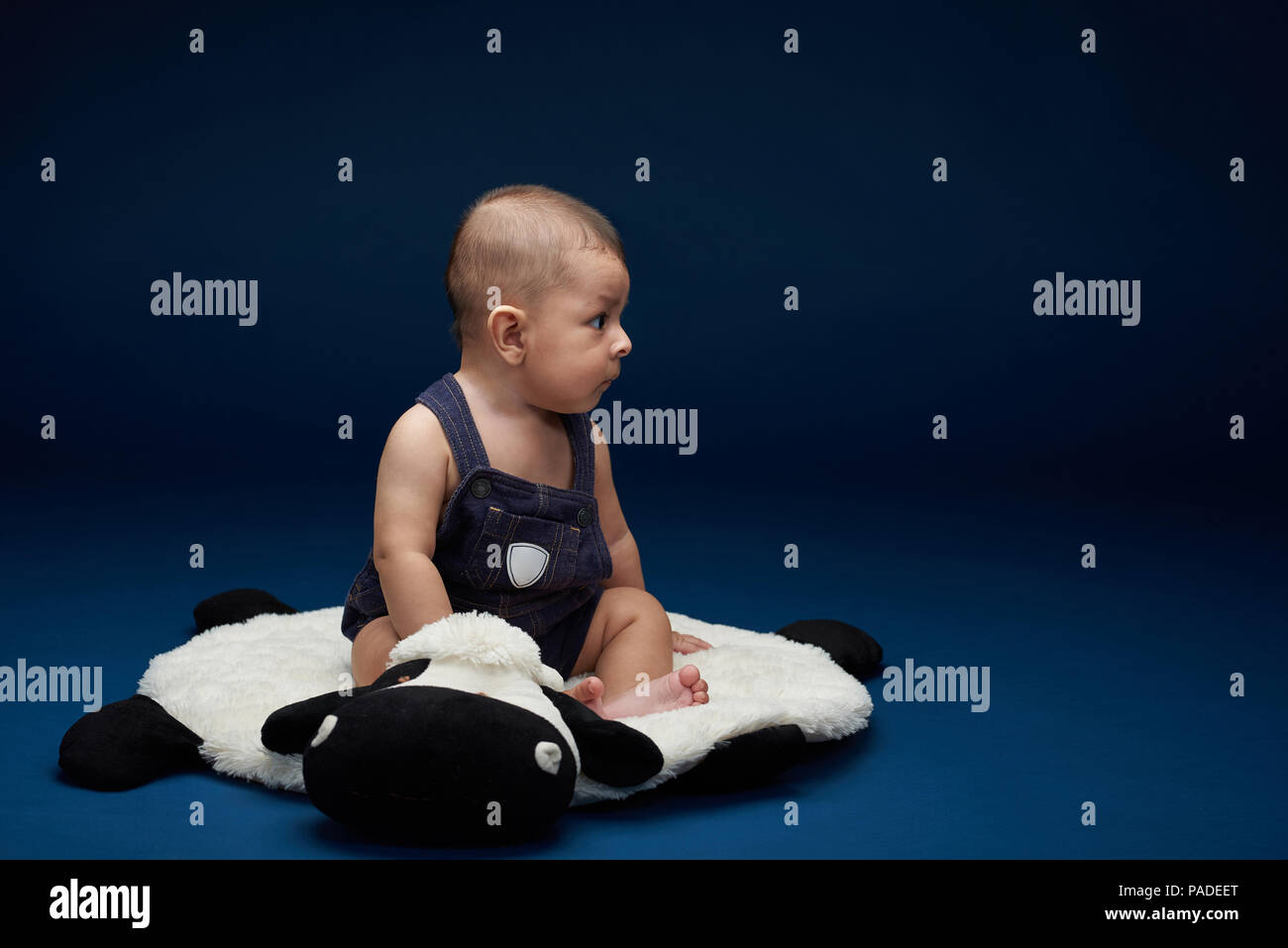 Baby look on side. Profile of cute sitting baby boy on blue studio background Stock Photo
