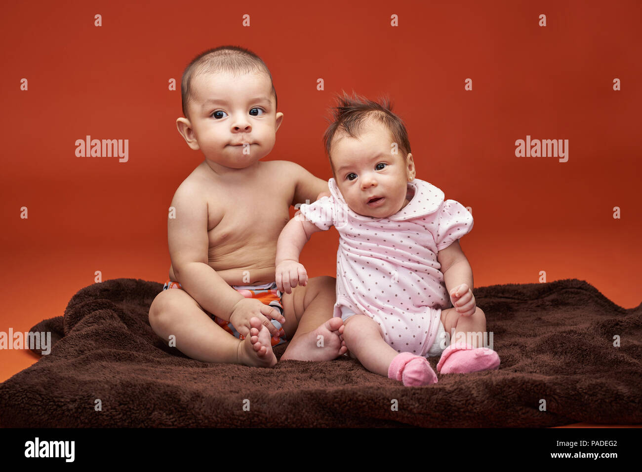 Two small baby kids portrait sitting on blanket isolated on orange color background Stock Photo