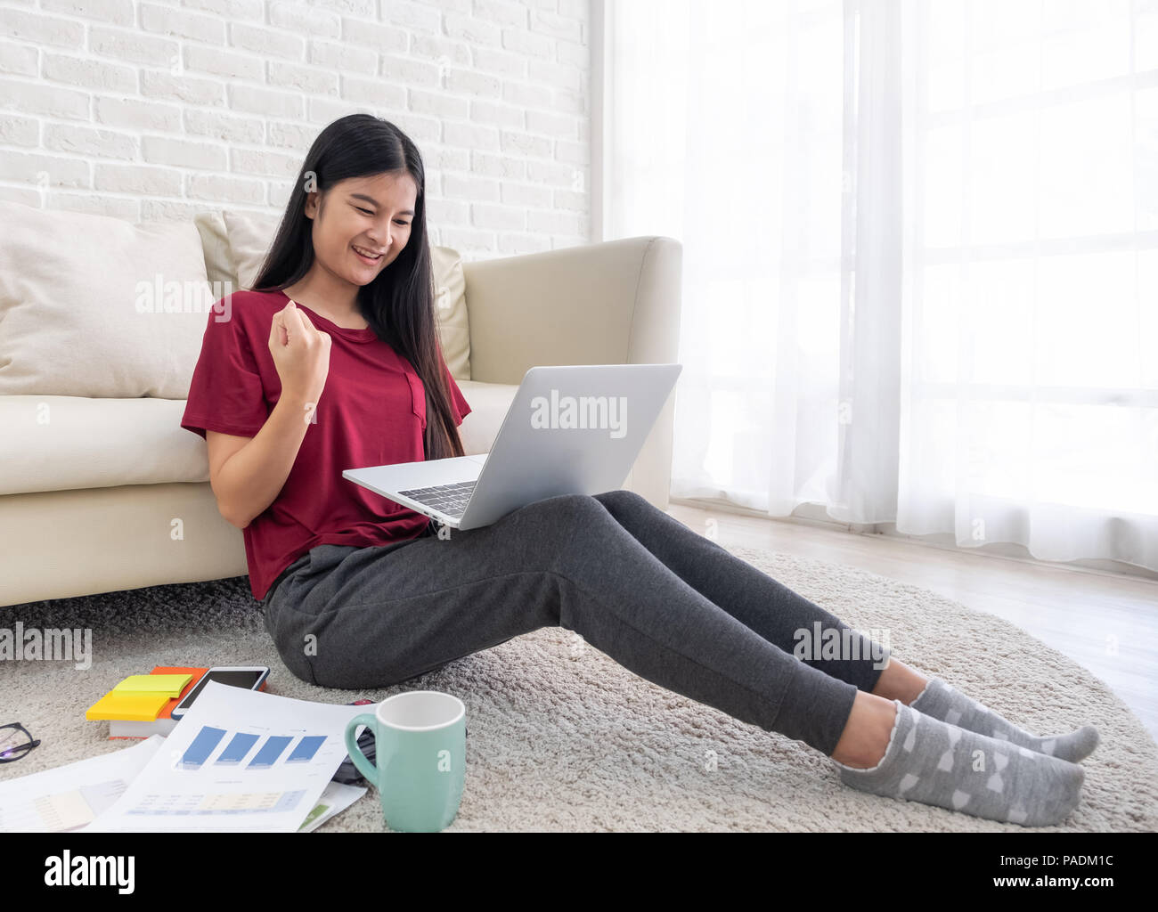 Asian woman freelancer hand up and smile for success working on laptop on sofa at home.work at home concept.yeah emotion Stock Photo