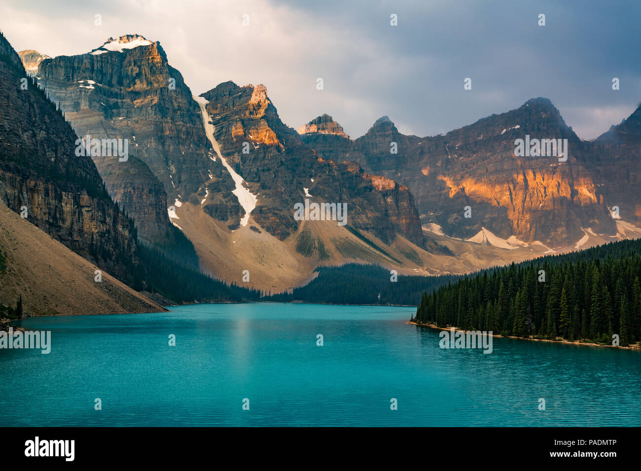 Sunrise with turquoise waters of the Moraine lake with sin lit rocky mountains in Banff National Park of Canada in Valley of the ten peaks. Stock Photo