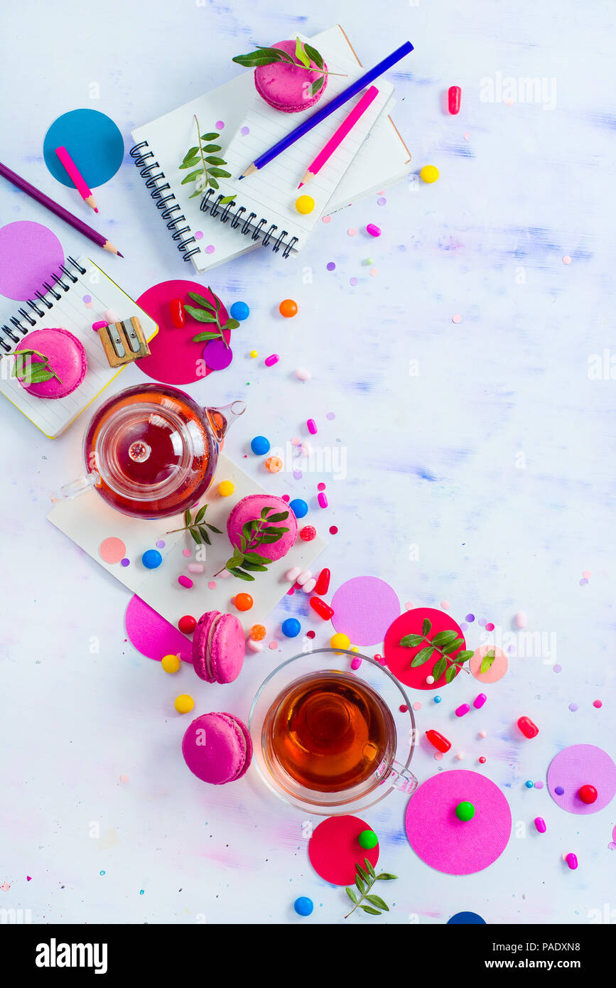 Glass teapot with candies and confetti on a light background with copy space. Pink and purple palette still life. Vibrant tea party drinks flat lay. Stock Photo
