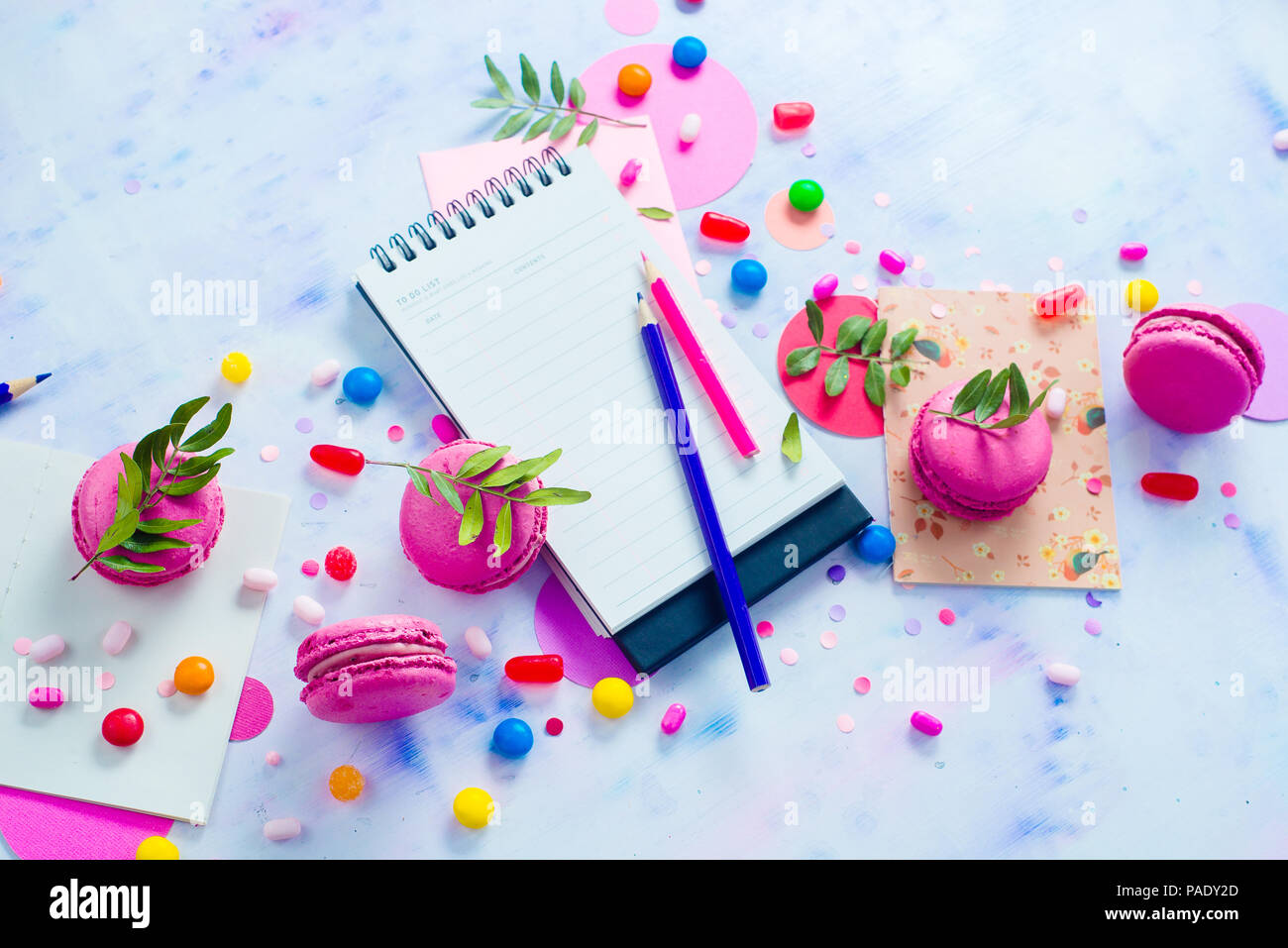 Party flat lay with confetti. To-do list with stationery, candies and macaroon cookies on a white wooden background. Colorful objects in high key with copy space. Stock Photo