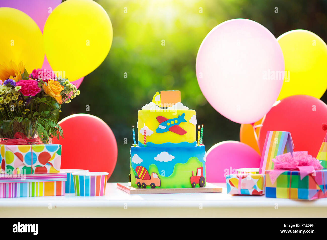 Kids birthday party decoration. Colorful cake with candles. Car and transportation theme boys party. Decorated table for child birthday celebration. R Stock Photo