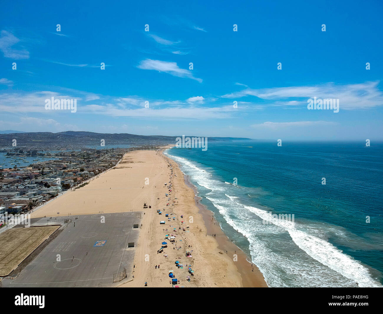 A California Beach lined with those looking to soak up the warm coast sun and splash in the cool Pacific Ocean. Image captured from an aerial drone at Stock Photo
