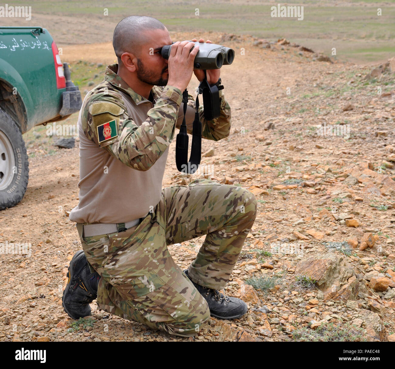 An Afghan Tactical Air Controller looks through binoculars at the