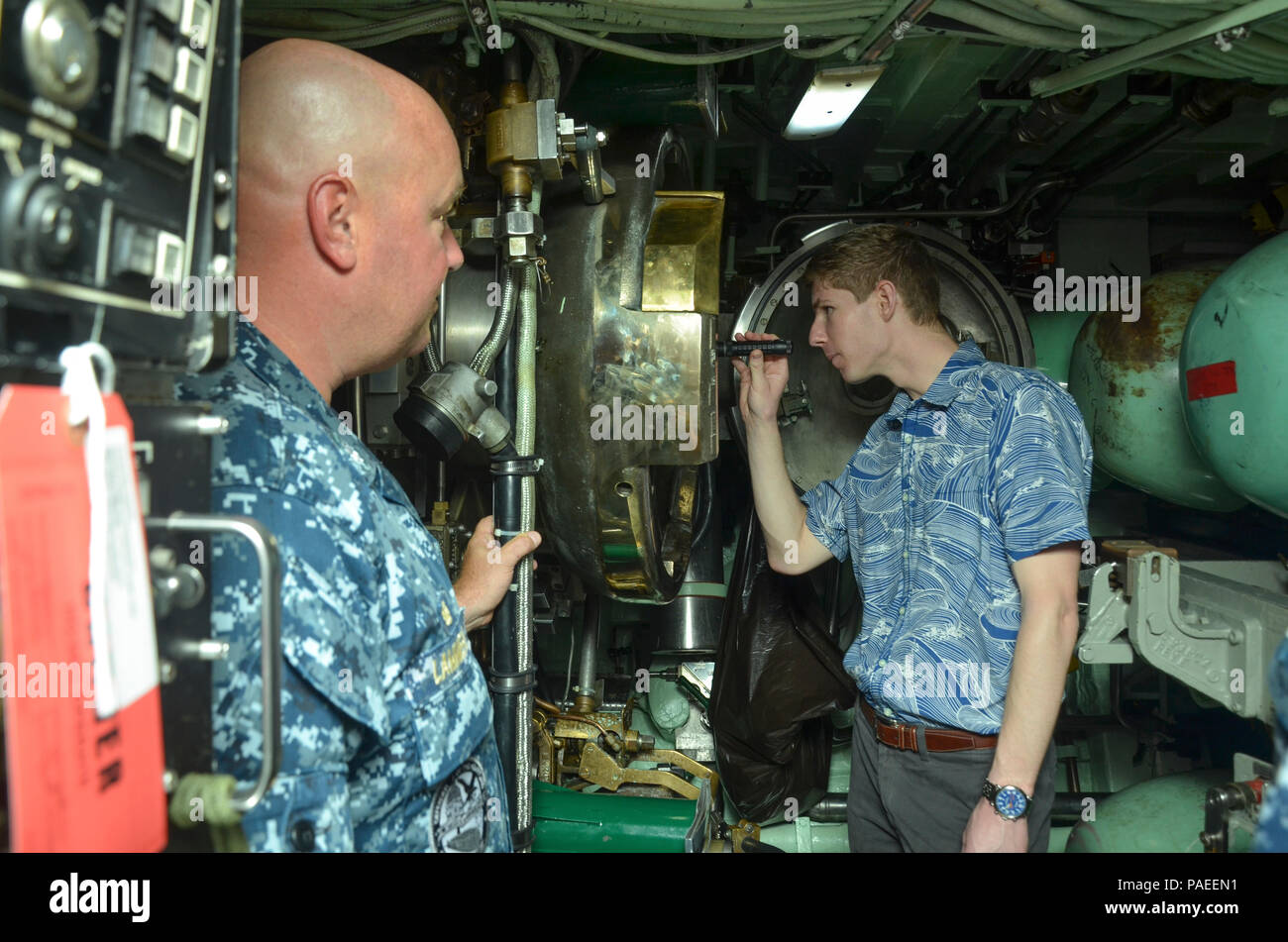 POLARIS POINT, Guam (March 30, 2016) —  Cmdr. David Lammers, commanding officer of the Los Angeles-class fast attack submarine USS Topeka (SSN 754), watches as guest civilian Will Rogers, a military legislative assistant, looks down a torpedo tube in the torpedo room, March 30.  Topeka is currently alongside the Emory S. Land-class submarine tender USS Frank Cable (AS40). Frank Cable, forward deployed to the island of Guam conducts maintenance and support of submarines and surface vessels deployed to the U.S. 7th Fleet area of responsibility.  (U.S. Navy photo by Mass Communication Seaman Appr Stock Photo
