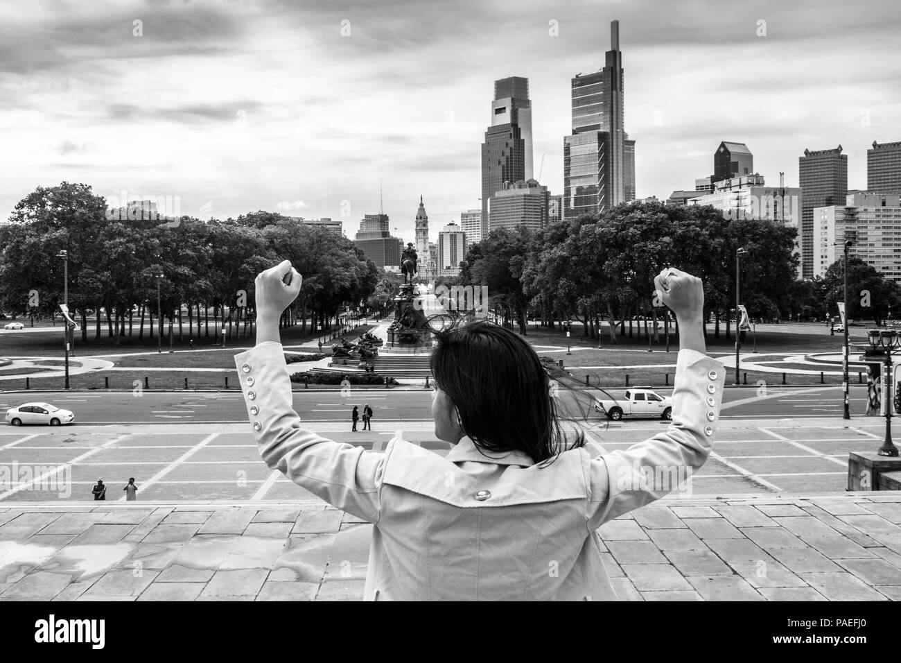 A young woman flexing and imitating the famous Rocky pose as a symbol of women empowerment - Rocky Steps, The Oval, Philadelphia, USA Stock Photo