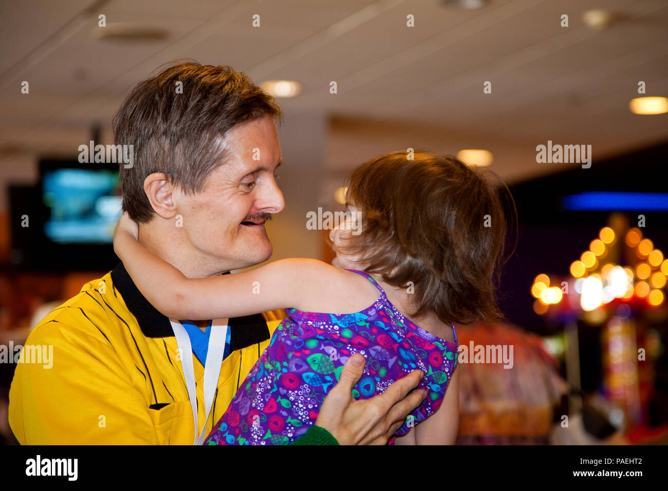 An adult man with Downs Syndrome holds his great niece as if they are dancing.  The two are looking at each other with smiles.  She is swinging in his Stock Photo