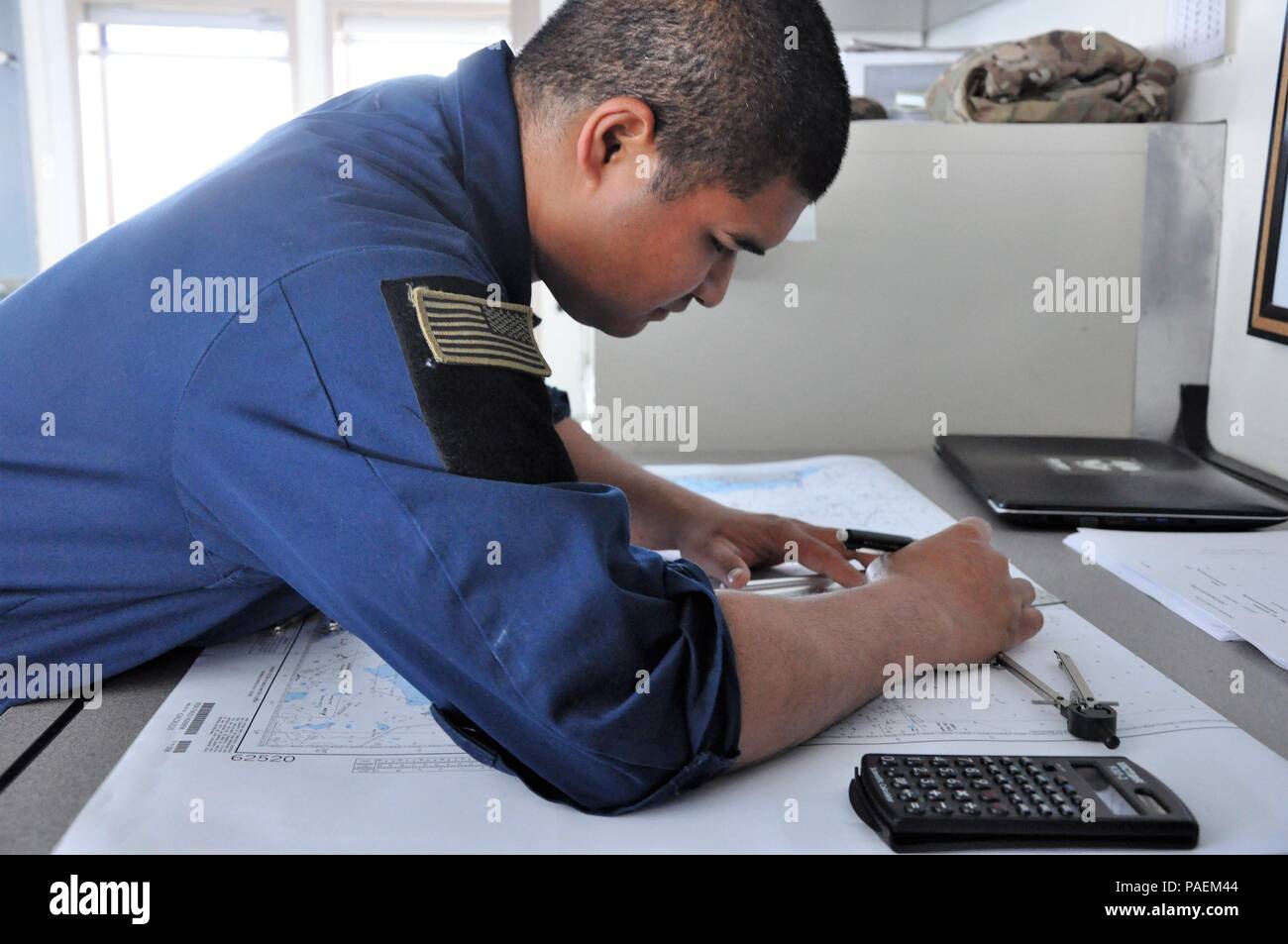 Sgt. Asau Asanuma, a watercraft operator and a lead seaman with the 1099th Transportation Detachment assigned to the SP4 James A. Loux, Logistics Support Vehicle-6, updates the vessel’s charts during a mission in the Persian Gulf, March 1, 2016.    Paper records of navigation charts are used in case of power or computer failure. Stock Photo