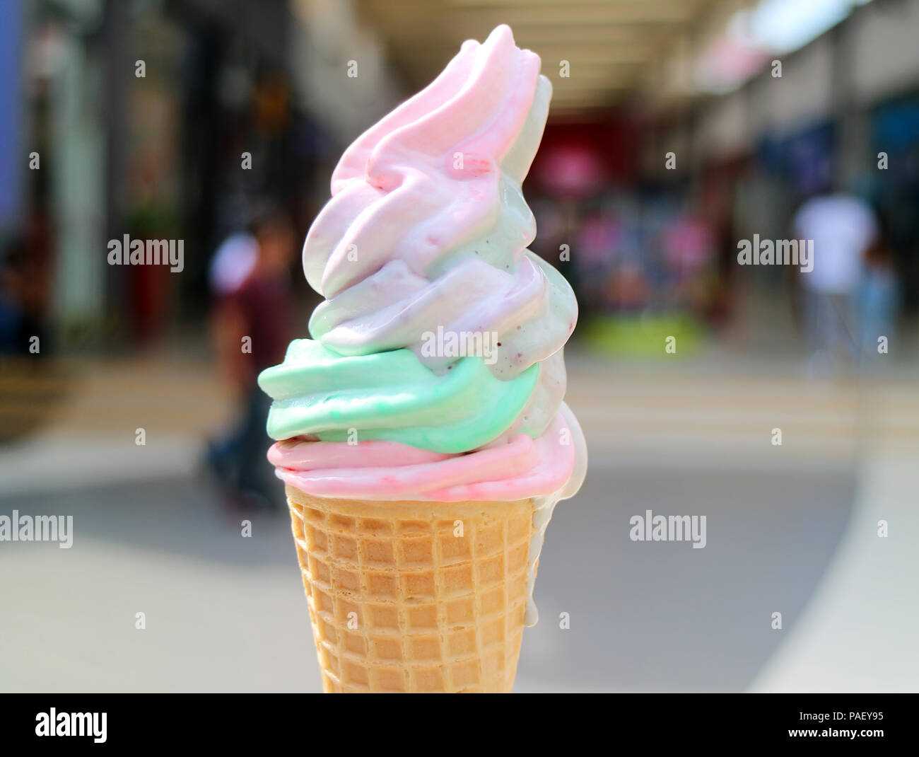 Melting Pastel Color Soft Serve Ice Cream Cone with Blurred Shopping Arcade in Background Stock Photo