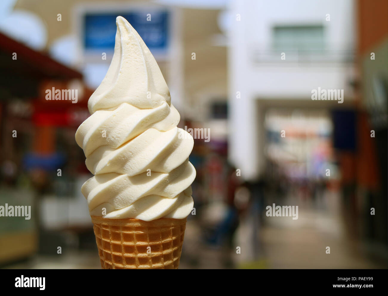 Front view of vanilla milk soft serve ice cream cone in the sunlight, with blurred city center view in background Stock Photo