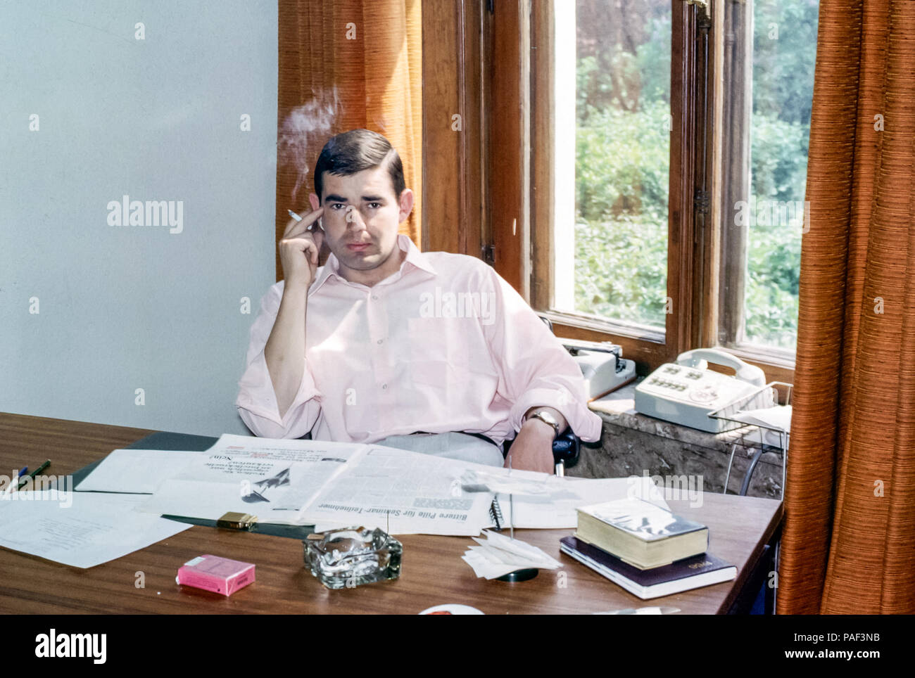 A Male Employee Sitting At A Desk With A Newspaper Smoking A