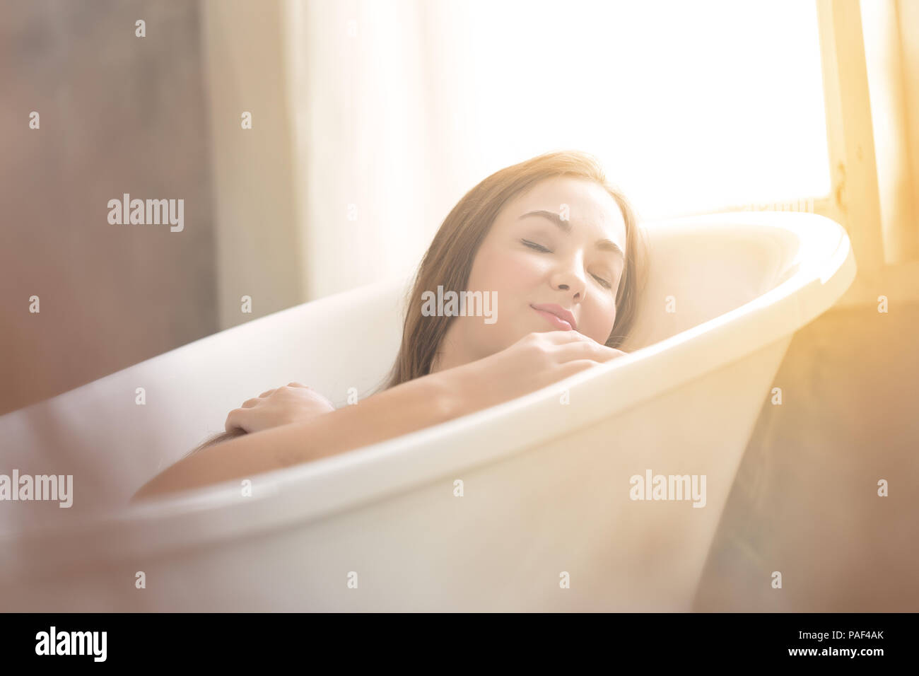 Beautiful young girl in the bathroom lie down in a bathtub with copy