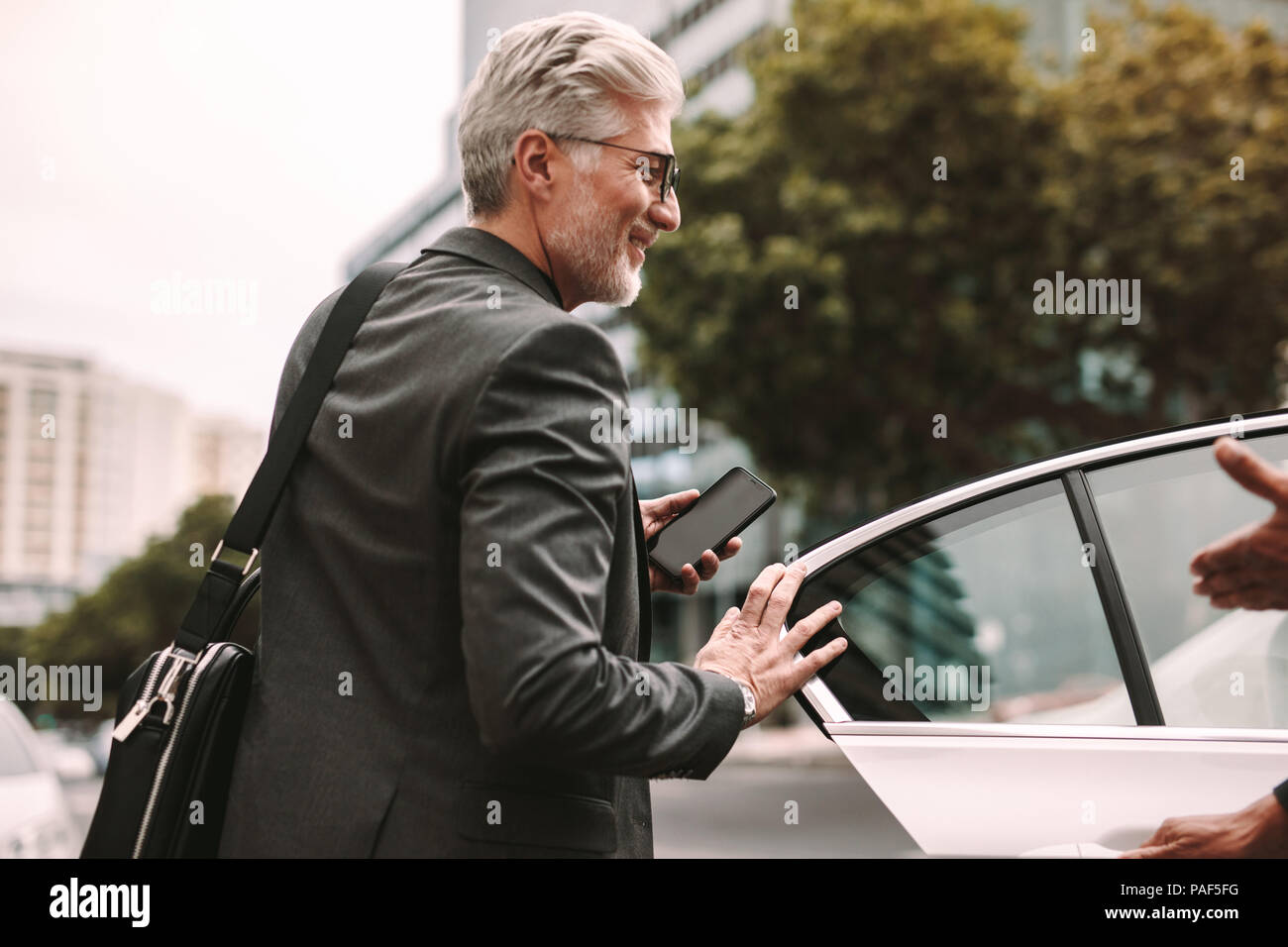 Happy mature commuter getting into a taxi. Businessman entering a taxi with driver opening door. Stock Photo