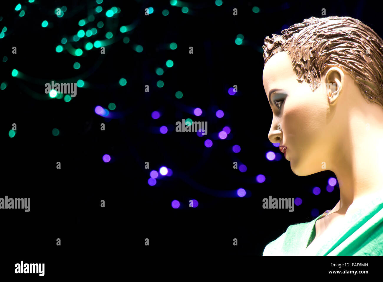 Close up of one female mannequin doll displayed n the shop window with blurred green and purple lights in the backgrd , profile view Stock Photo