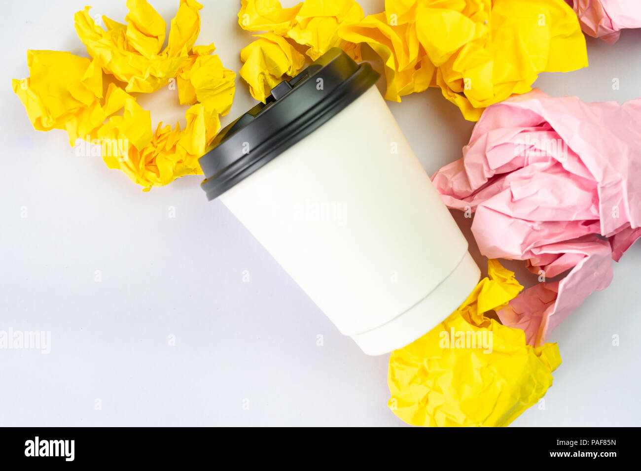 white coffee cup with colourful crumbled paper balls on white ...