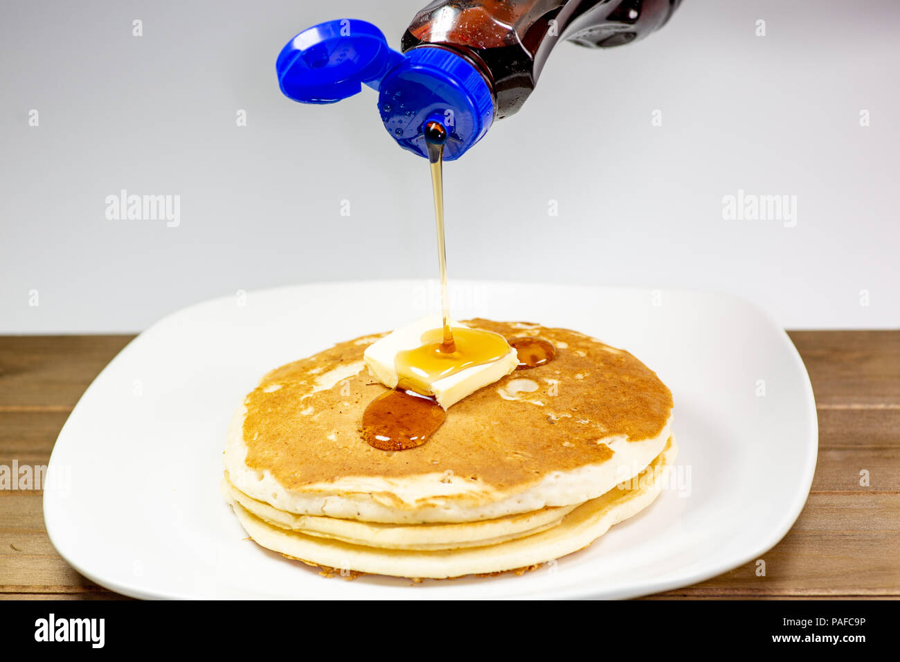 Pouring syrup from a blue tip bottle onto the square of butter on a