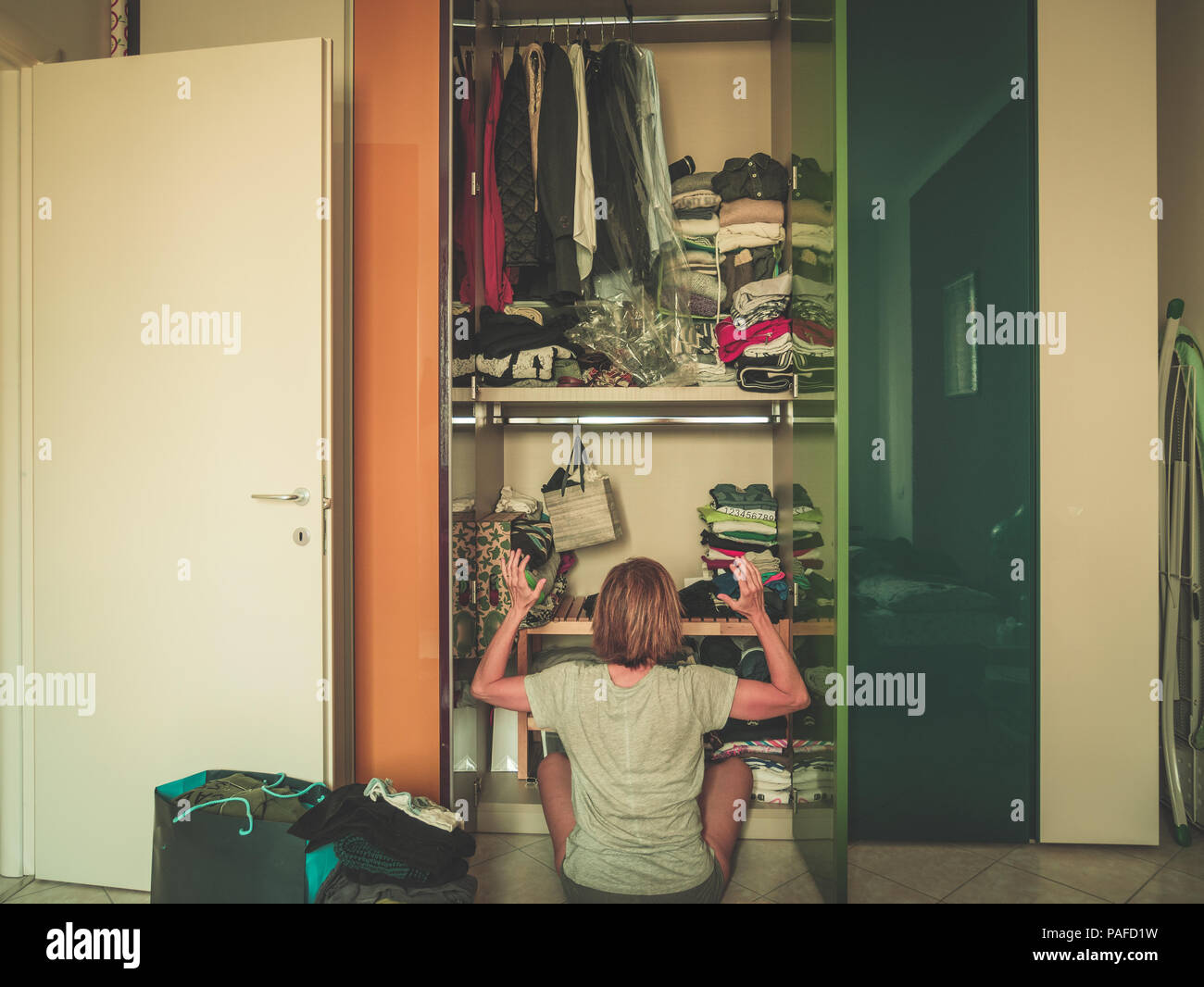 Woman looking at wardrobe, home interior, desperate housewife, cleaning home, rear view sitting, toned vintage style. Stock Photo