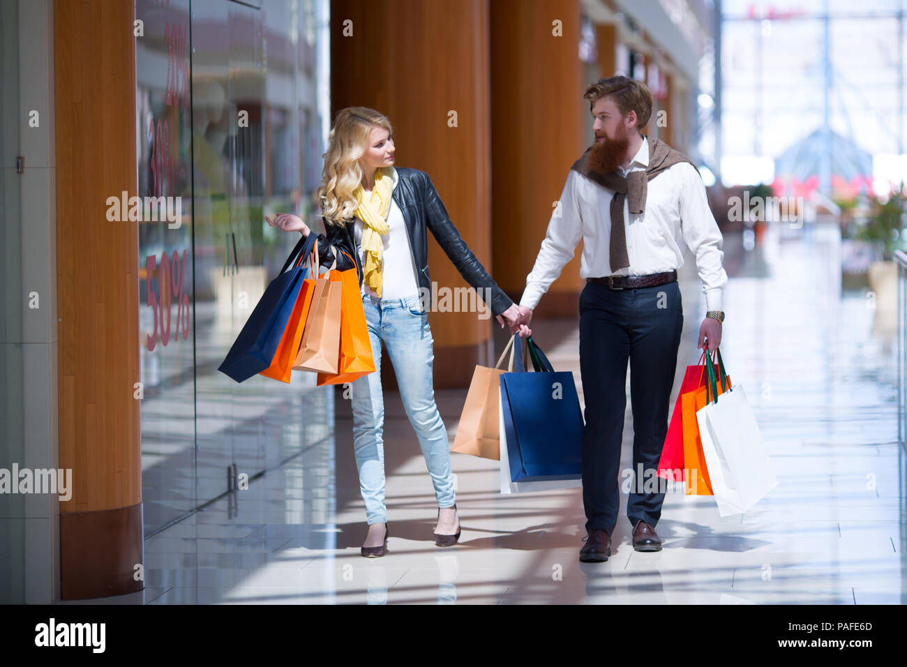 Happy beautiful young couple with shopping bags walking holding hands in mall Stock Photo