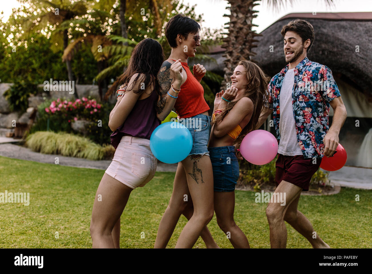 Group of friends playing balloon popping race at party. Men and women trying to burst the balloon of each other. Stock Photo