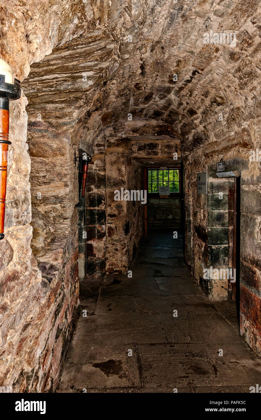 A medieval stone vaulted passage with openings, leading to an ancient dark cross corridor and doorway fitted with a wide window protected by iron bars Stock Photo