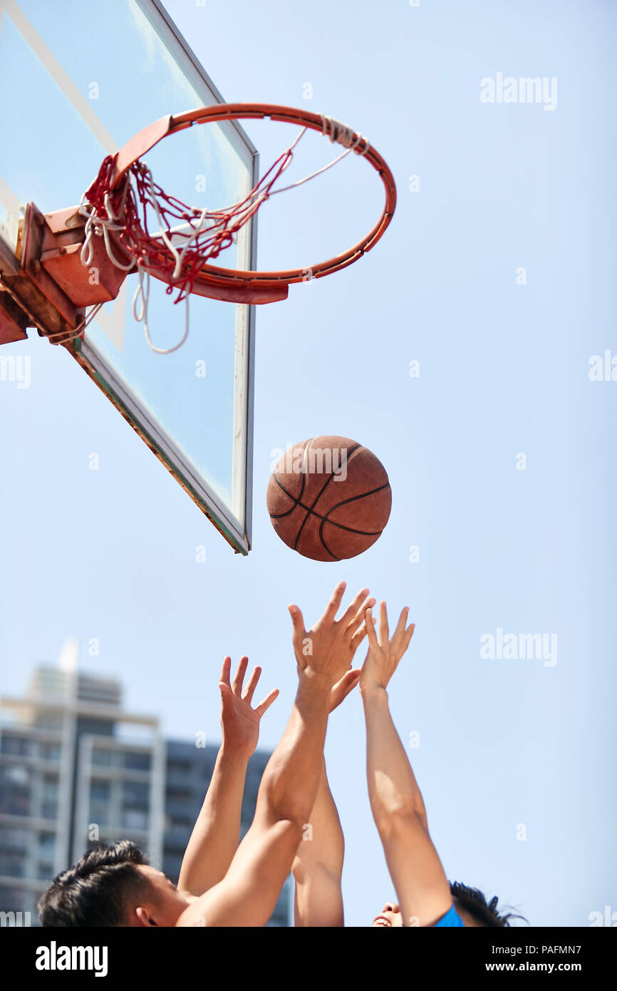 young asian adults going up for rebounds on outdoor basketball court. Stock Photo
