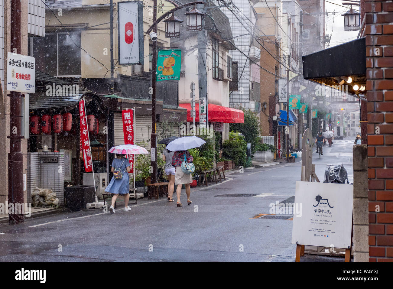 Three young women under umbrellas walking through a Tokyo street scene in summer rain Stock Photo