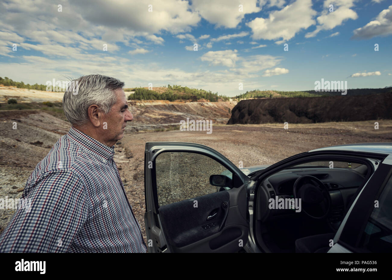 Open car door with elderly man standing looking at the dashboard with zaranda mines in the background, Spain Stock Photo