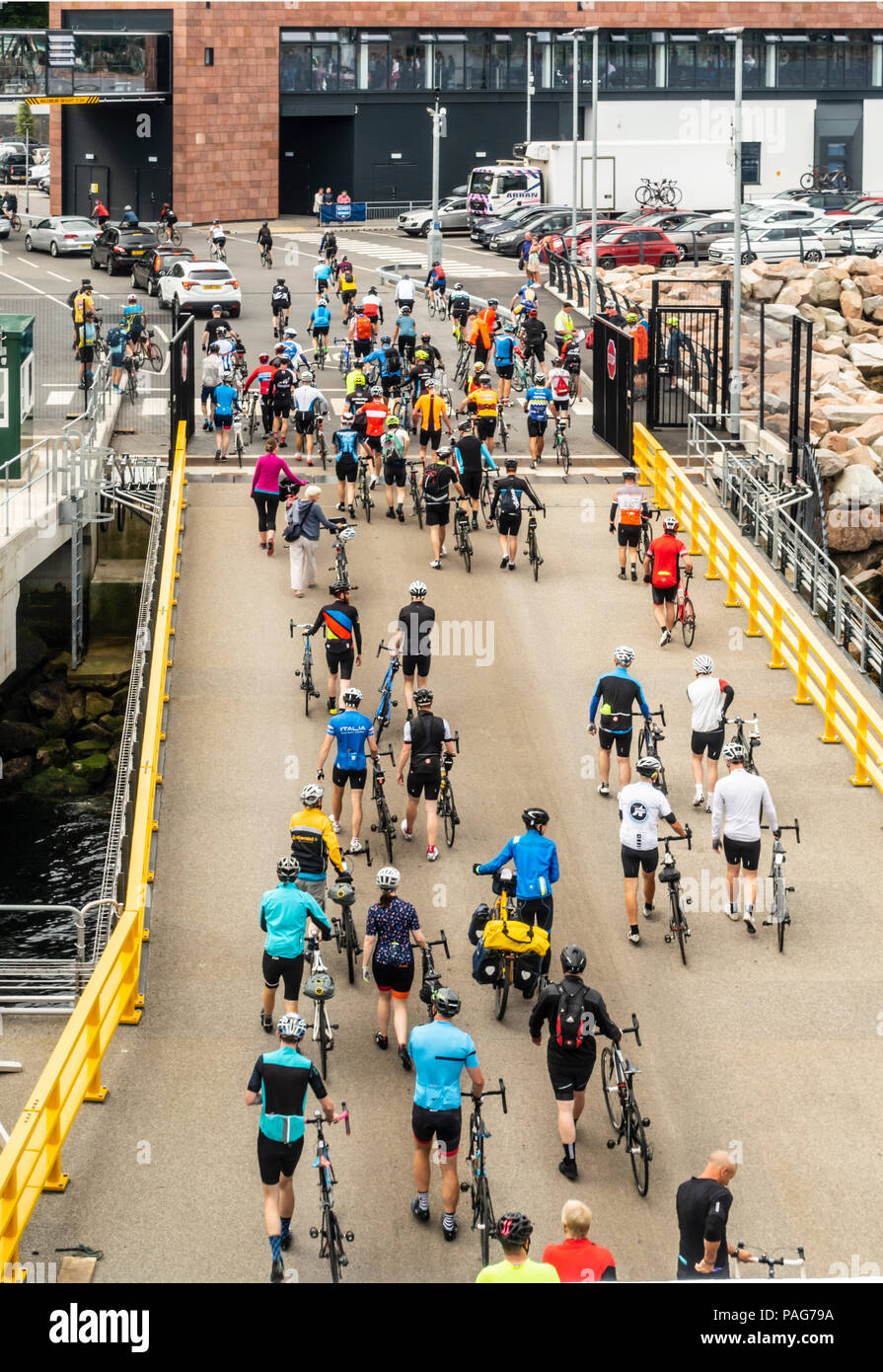 Cyclists walking their bicycles up the car ramp at the new (2018) ferry terminal at Brodick pier, Isle of Arran. Cars can be seen leaving and waiting Stock Photo