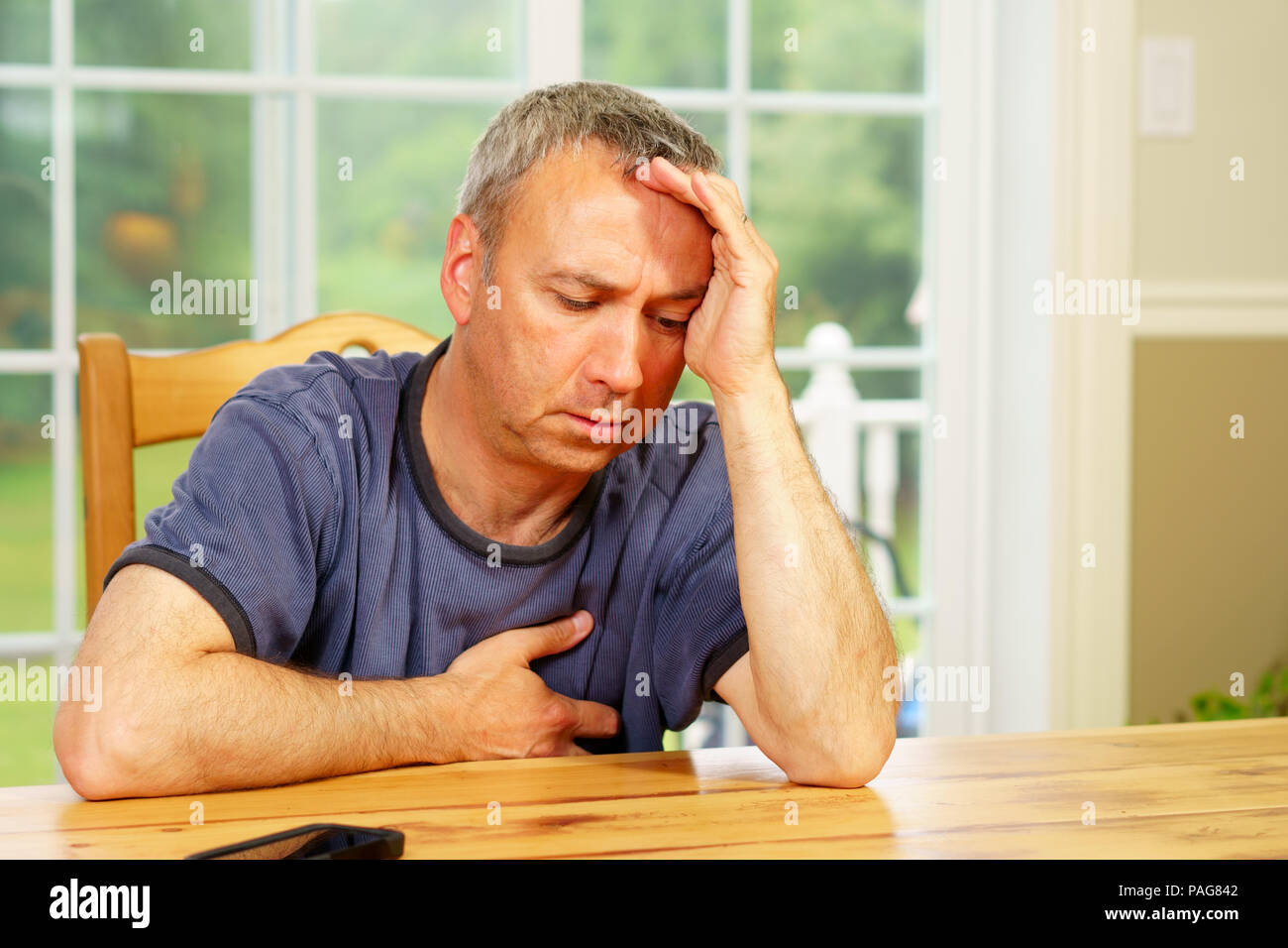 Caucasian man, alone, sit at a table, day, worrying about his situation. Questionning himself. Stock Photo