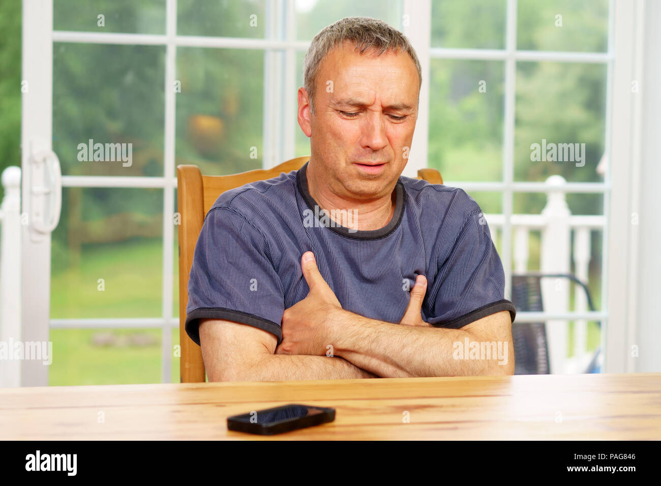 Caucasian man, alone, sit at a table, day, worrying about his situation. Questionning himself. Stock Photo