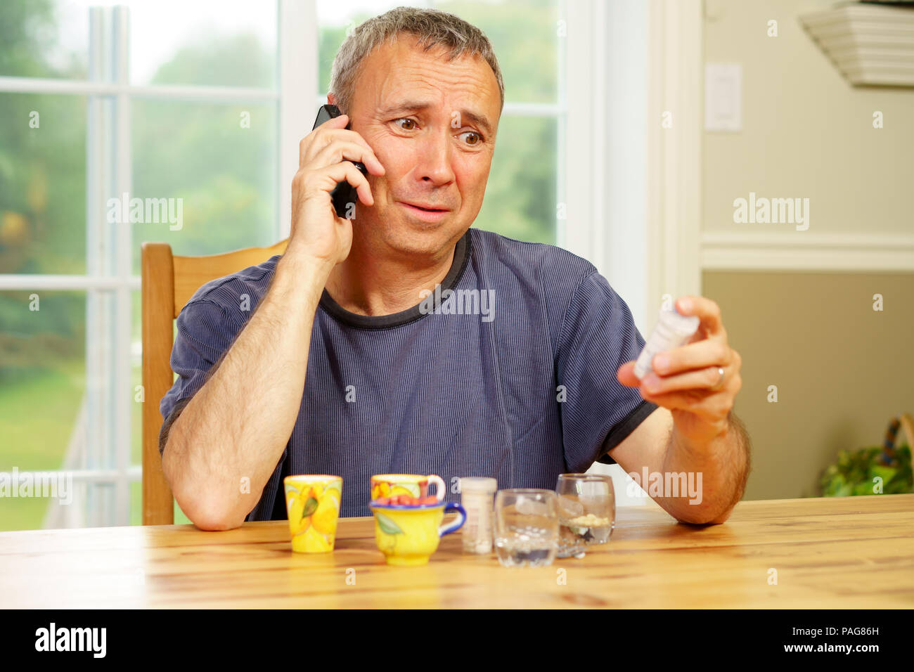 Caucasian man, alone, sit at a table, day, worrying about the pills he is supposed to take. Stock Photo